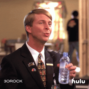 A young blond man shaking as he tries to drink water, spilling it all over himself.